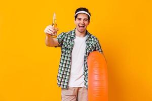 homem positivo com roupa de verão sorrindo e posando com garrafa de cerveja e círculo inflável