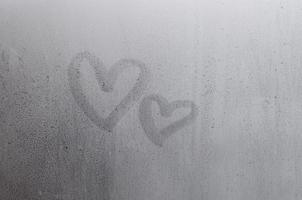 par de símbolo de coração de amor turva abstrato desenhado à mão no vidro da janela molhada com fundo de luz solar. modelo para cartões postais de dia dos namorados foto
