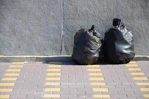 dois sacos de lixo pretos no chão da rua de azulejos na cerca de concreto na cidade foto