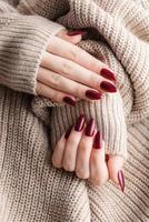 mãos de uma jovem com manicure vermelho escuro nas unhas foto