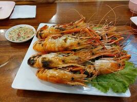 vários camarões grelhados foram servidos em um prato branco com molho de frutos do mar no restaurante. foto