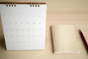 página do calendário fechar no fundo da mesa de madeira com conceito de reunião de compromisso de planejamento de negócios de caneta e caderno foto