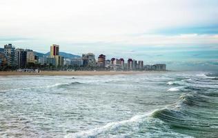 bela vista da praia da cidade costeira do lado do mar agitado com montanhas ao fundo foto