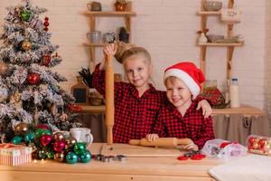 duas crianças um menino e uma menina cozinham biscoitos para o natal em casa na cozinha foto