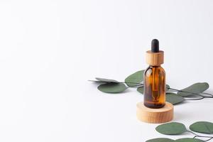 frasco cosmético com um pódio de madeira com eucalipto em fundo branco. close-up, copie o espaço foto