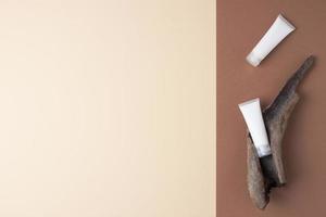 tubos brancos de creme cosmético com madeira em fundo marrom e bege. postura plana, copie o espaço foto