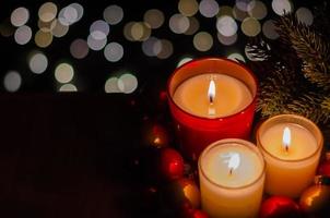 foco e turva de velas acesas com árvore de natal e enfeites de bugiganga em bokeh claro e fundo escuro. foto