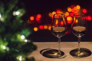 dois copos de vinho rosé na mesa de madeira com árvore de natal e luz de fundo colorida bokeh. foto