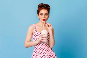 jovem pensativa bebendo bebida. tiro de estúdio da garota pinup gengibre desfrutando de milk-shake. foto
