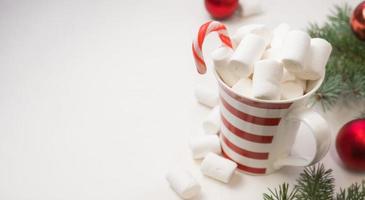 chocolate quente com marshmallows em uma padaria vermelha e branca em um fundo branco e galhos de uma árvore de ano novo. foto