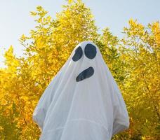 fantasma de halloween, dançando na floresta amarela de outono, acenando com as mãos. um fantasma alegre em um lençol branco. foto