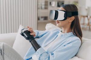 menina com deficiência em óculos vr interage com realidade aumentada, toca seu braço protético de alta tecnologia foto