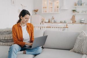 garota moderna trabalhando no laptop, fazendo compras online, conversando nas redes sociais, sentado no sofá em casa