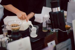 mulher barista preparando café com leite derrama leite em um copo. foto