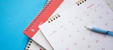 página do calendário com caneta close-up no conceito de reunião de compromisso de planejamento de negócios de fundo azul foto