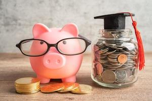 cofrinho usando óculos com moedas e chapéu de formatura, salvando o conceito de educação bancária. foto