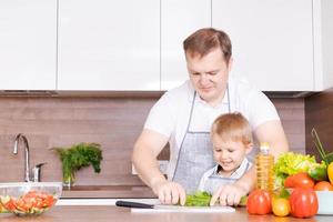 pai amoroso e filho pré-escolar cozinhando legumes cortados para salada foto