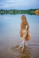 uma bela jovem esbelta em um vestido longo fica na água do lago foto