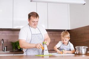 pai cozinha com seu filho, esfrega cenouras no ralador em casa na cozinha, tem foto
