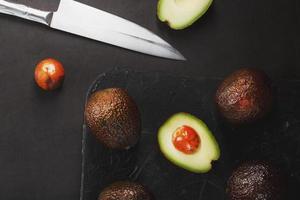 abacates maduros em uma cesta em uma mesa preta, com uma fruta cortada e uma pedra. foto