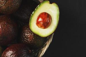 abacate hass maduro e uma fatia sem caroço em uma cesta em um plano de fundo texturizado preto. foto