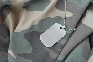 contas militares prateadas com placa de identificação no uniforme de fadiga de camuflagem foto