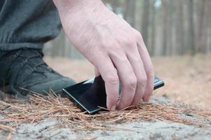 mão masculina pegando o celular perdido de um chão no caminho de madeira de abeto outono. o conceito de encontrar uma coisa valiosa e boa sorte foto