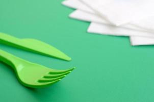 talheres de plástico descartáveis verdes. garfo e faca de plástico estão sobre uma superfície de fundo verde ao lado de guardanapos foto