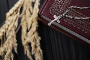 colar de prata com cruz crucifixo no livro da bíblia sagrada cristão na mesa de madeira preta. pedindo bênçãos de Deus com o poder da santidade foto