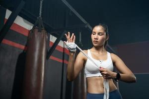 mulheres asiáticas adultas usando bandagem elástica para amarrar as mãos antes de colocar uma luva de boxe para aula de treinamento de boxeador, esporte, fitness e conceito de exercício para uma boa saúde e músculos e corpo fortes. foto