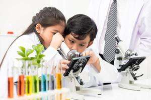 jovens crianças asiáticas vestindo vestido branco de cientista e fazem tubo de ensaio químico enquanto estudam, aprendendo na sala de aula de ciências com o professor. conceito de educação de crianças pequenas por experimento, diversão e diversão em sala de aula foto