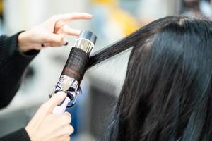 foco seletivo no equipamento de ondulação do cabelo elegante enquanto faz o cabeleireiro e coloca o tratamento de cuidados enquanto estiliza o cabelo encaracolado para o cliente. ocupação profissional, serviço de beleza e moda. foto