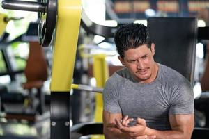 homens caucasianos adultos jovens se sentindo dolorosos por lesão muscular no ombro após treino com máquina de levantamento de peso dentro da academia de ginástica. músculo lesionado de treino ou exercício para musculação. foto