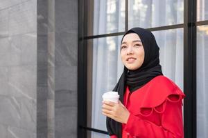 belas mulheres islâmicas do leste asiático usando hijab com vestido formal. segurando a xícara de café e andando na área urbana da cidade, sentindo-se feliz e sorrindo. conceito de estilo de vida de pessoas com espaço de cópia.