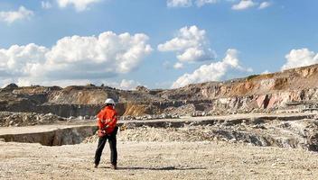 tiro de paisagem de rocha e mina de concreto que cercam com pedra, montanha e céu azul. com engenheiro industrial que monitora o trabalhador que dirige caminhão e máquina de perfuração. conceito industrial. foto