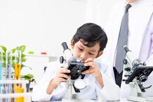 jovem estudante de elemento asiático ajusta e usa microscópio na aula de ciências para examinar o assunto da vida com o professor. educação e crianças aprendendo ou experimentando no conceito de sala de aula. foto