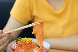 mulher asiática comendo sashimi fatia de salmão com arroz no restaurante japonês foto