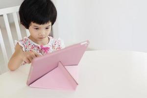 menina asiática jogando tablet digital em casa foto