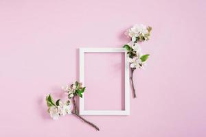 quadro em branco branco com espaço de cópia encontra-se em um fundo rosa cercado por ramos florescentes de uma macieira. conceito de anúncio de primavera foto