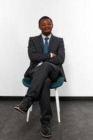 homem negro afro-americano sorridente em terno de negócios, sentado na cadeira com os braços cruzados foto
