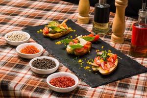 um close da mesa de servir com saborosos sanduíches ou bruschetta com legumes e especiarias no quadro negro foto