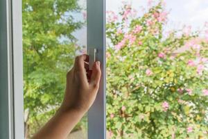 mão segure a alça da tela de arame da rede mosquiteira na janela da casa foto