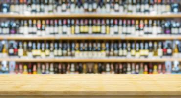 tampo de mesa de madeira vazio com garrafas de vinho borradas nas prateleiras de álcool de licor no fundo da loja de vinhos do supermercado foto