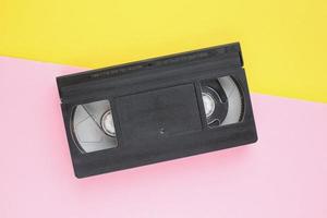 cassete de fita de vídeo vhs preta sobre fundo amarelo e rosa. velha tecnologia obsoleta para gravação em fita e assistir a filmes de mídia. retrô, vintage, história, conceito de nostalgia. vista superior, configuração plana foto