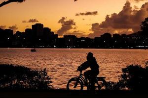 rio de janeiro, rj, brasil, 2022 - pessoas correndo e andando de bicicleta em silhueta ao pôr do sol na lagoa rodrigo de freitas foto