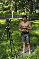 yogi masculino bonito ativo desenho tablet andando na floresta antes ou depois de um treino. aula de ioga jovem hispânico atlético com um tapete de fitness foto