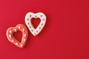 dois decorados com glacê e biscoitos em forma de coração vitrificado no fundo vermelho com espaço de cópia. conceito de comida de dia dos namorados foto