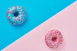 dois donuts em um fundo rosa pastel e azul. composição de comida criativa de minimalismo. estilo plano leigo foto