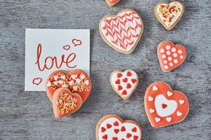 biscoitos decorados e vitrificados em forma de coração e nota de papel com inscrição amor no fundo cinza, vista superior. conceito de dia dos namorados foto