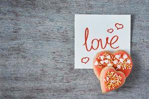 biscoitos decorados e vitrificados em forma de coração e nota de papel com inscrição amor no fundo cinza, vista superior. conceito de dia dos namorados foto